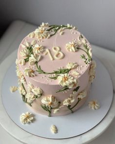 a pink cake with white flowers and the number eighteen on it is sitting on a plate