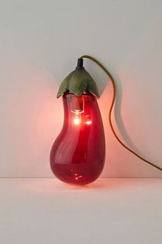 a red vase with a green leaf on it sitting next to a light bulb that is turned on