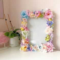 a white table topped with a mirror covered in colorful paper flowers next to a potted plant