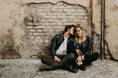 two people sitting on the ground next to each other near a brick wall and street sign