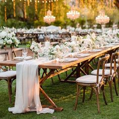 a long wooden table with white flowers and greenery is set up for an outdoor dinner