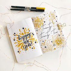 an open happy new year notebook with fireworks on it next to a pen and marker