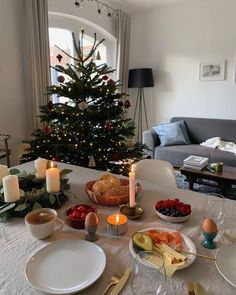 a christmas tree is lit in the living room with food and candles on the table