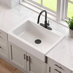 a white kitchen sink sitting under a window next to a potted plant on top of a counter