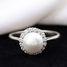 a white pearl and diamond ring on a black surface