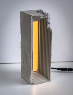 a concrete sculpture with a yellow light coming out of the center and inside it, sitting on a white surface next to a black cord