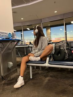 a woman sitting on a bench with headphones in her ears at an airport terminal