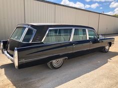 an old black station wagon parked in front of a building with no doors on it