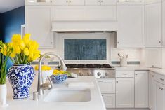 a kitchen with white cabinets and yellow flowers in vases