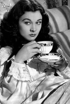 a woman sitting on a couch with a cup and saucer in her hand while holding a plate