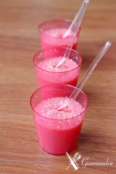 three glasses filled with pink liquid on top of a wooden table next to two straws