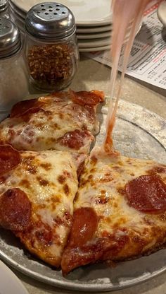 two slices of pepperoni pizza are being cut by a spatula on a plate