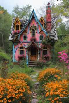 a pink and blue house in the middle of some flowers with lots of greenery around it