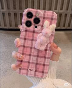 a person holding up a pink plaid phone case with a teddy bear on the back