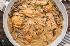 chicken and mushroom stew in a white bowl on top of a wooden table with utensils