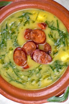 a bowl filled with soup and sausages on top of green beans next to a spoon