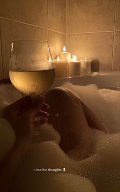 a person is taking a bath with candles in the water and wine glasses on the side