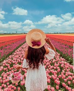 a woman in a hat standing in a field of tulips