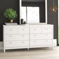 a white dresser with a mirror and potted plant on top in a black room