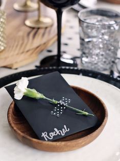 a table setting with black napkins and white flowers in a wooden bowl on the plate