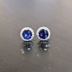 These beautiful stud earrings feature a pair of 2.24-carat weight Ceylon sapphire gemstones with natural earth-mined diamonds, all set in solid 14K gold. These earrings can be a lovely September birthstone gift for your loved ones! As listed, these earrings are ready to ship. If you're interested in purchasing this setting with a different center stone please message us! Sapphire Diamond Earrings With Gemstone Detail, Sapphire Round Cut Earrings With Halo Design, Sapphire Earrings With Halo Design, Sapphire Halo Design Round Cut Earrings, Sapphire Diamond Round Cut Earrings, Sapphire Diamond Earrings With Round Cut, Sapphire Diamond Earrings With Halo Design, Sapphire Round Cut Earrings With Halo Setting, Sapphire Earrings With Halo Setting