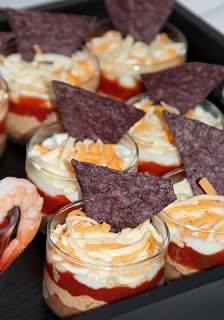 small desserts are arranged on a tray with chips and dips in the middle