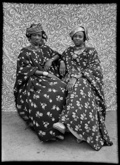 two women sitting next to each other in front of a wall