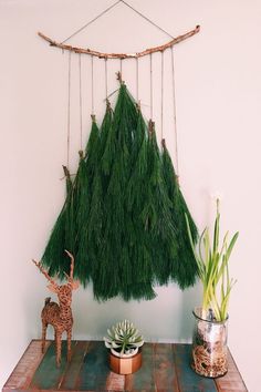 a small deer statue next to a fake christmas tree hanging from a rope on a wall