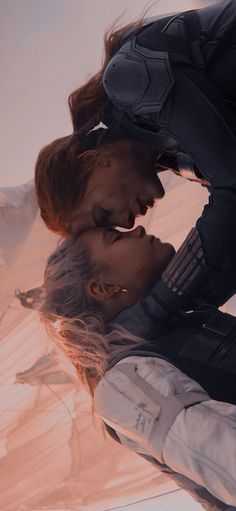 two people are kissing in front of a desert background with the sun shining on them