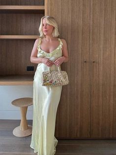 a woman in a white dress holding a purse standing next to a wooden bookcase