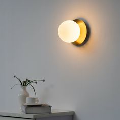 a white vase sitting on top of a table next to a wall mounted light fixture