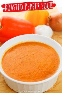 roasted pepper soup in a white bowl on a wooden table with peppers and garlic around it