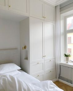 a white bed sitting next to a window in a room with lots of cupboards