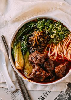 a bowl filled with meat, noodles and veggies next to chopsticks