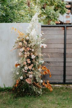 an arrangement of flowers in front of a wooden fence on the side of a house