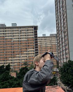 a young boy looking up into the sky with buildings in the background