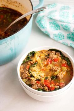 a white bowl filled with meat and vegetables next to a blue casserole dish