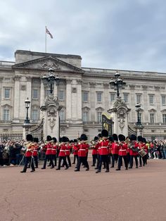 a group of men in red jackets and black pants marching past a building with flags on it