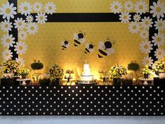 a table topped with lots of cake and flowers next to a wall covered in bees