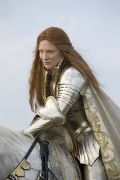 a woman dressed in armor riding on the back of a white horse with long red hair