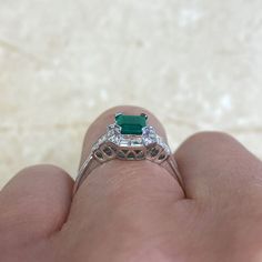 A geometric gemstone and diamond ring that features a lively natural emerald with a green saturation. Surrounding the center diamond is a halo of baguette-cut diamonds and round-cut diamonds. Additional baguette-cut diamonds are set on the shoulder. This ring is handcrafted in 14k white gold.
The approximate emerald weight of this ring is 0.79 carats. The total approximate diamond weight of this ring is 0.54 carats.
The measurements of this ring including the halo are approximately 9.60mm x 8.35 Emerald Ring With Baguette Diamonds And Asscher Cut, Baguette Cut Emerald Ring For May Birthstone, Emerald Ring With Baguette Diamonds Fine Jewelry, Emerald Ring With Baguette Diamonds In Fine Jewelry Style, Art Deco Emerald Cut May Birthstone Ring, Emerald Cut Emerald Ring With Baguette Diamonds, Green Baguette-cut Platinum Jewelry, Art Deco Emerald Cut Emerald Ring For May Birthstone, Green Baguette-cut Art Deco Jewelry