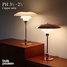 two lamps sitting on top of a wooden table next to a lamp that reads ph 3 2 / 2 - 2 / 2 copper table