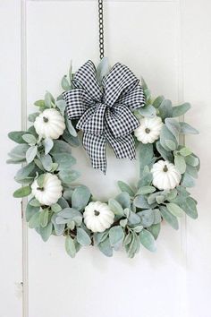 a wreath with white pumpkins and greenery hangs on a door handle that is decorated with black and white gingham ribbon