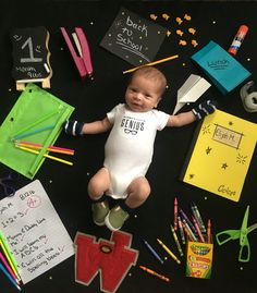 a baby laying on the floor surrounded by school supplies