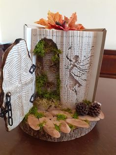 an open book sitting on top of a table covered in moss and pineconis