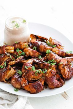 a white plate topped with chicken wings and garnished with scallions next to a jar of ranch dressing