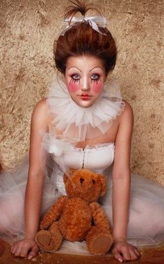 a woman with makeup on her face sitting next to a teddy bear wearing a tutu