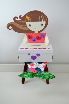 a paper doll sitting on top of a table with a card in it's lap