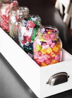 jars filled with candy sitting on top of a wooden table next to a metal drawer