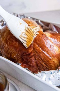 a plastic brush brushing off the top of a baked turkey in tin foil on a counter